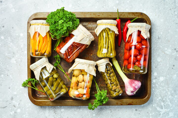 Assortment of pickled vegetables in a glass jar. Food supplies. On a stone background. Top view.