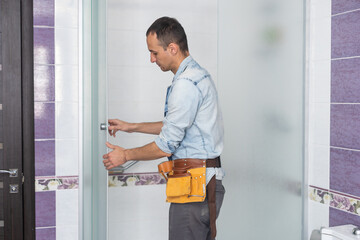 Workers are installing a silicone gasket seal on the glass door of the shower enclosure.
