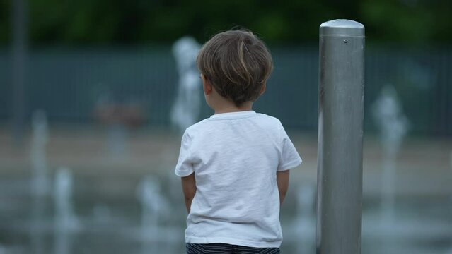 Back of a little boy looking at public fountain water jets erupting