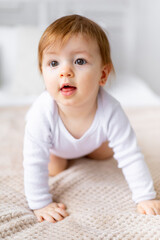 a small child girl learns to crawl on a bed in a bright room on cotton white linen, close-up portrait
