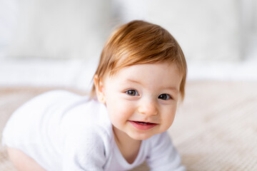 close-up portrait of a cute little baby girl in a bright room in white clothes at home on a bed, the concept of children's goods
