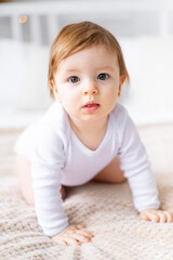 a close-up portrait of a cute little child in a bright room in white clothes at home on a bed, the concept of children's goods