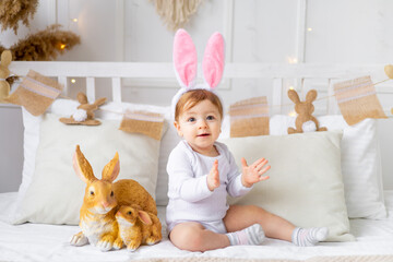 baby girl in bunny ears on the bed at home with painted eggs and rabbit, easter concept, cute Easter baby is waiting for the holiday and rejoicing