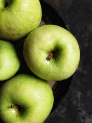 Close up green apples in retro plate on black concrete background. Flatlay with summer fruit and water drops. Granny smith.