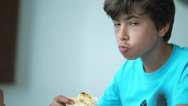 Candid young boy eating piece of pizza with family lunch