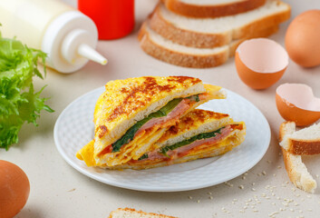 Gourmet Ham sandwich with eggs, cheese, tomato sauce or ketchup, mayonnaise and lettuce. Delicious healthy Breakfast on a gray plate on a light stone background. Selective focus