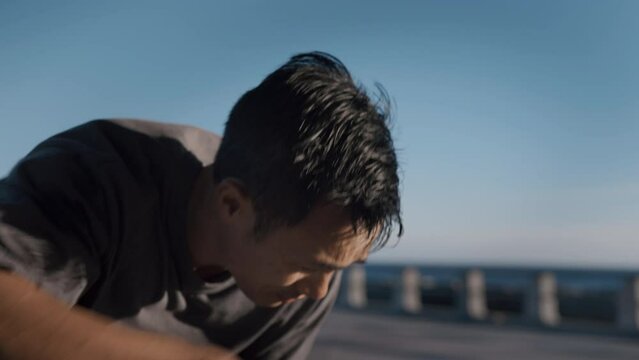 Attractive handsome tired sporty man has rest after intense workout, running exercise, gym training, fitness class outdoor, outside near water of sea, ocean during warm sunny day on sunny weekend