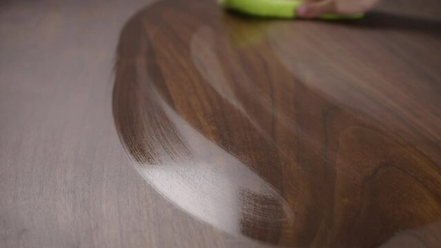 Man wet wiping walnut wood table with special solution closeup