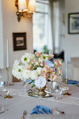 Blue wedding decor. Festive table decorated with flowers on the center, candles, silverware and plates with silk napkins on dusty blue tablecloth
