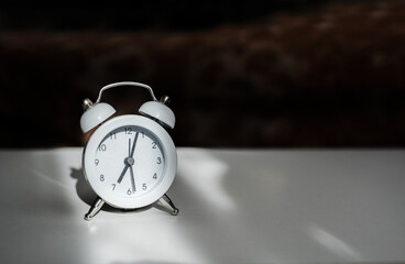 white vintage alarm clock shows 7 am on the dial on a white table close-up