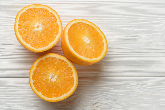 Three Halves Of An Orange On A White Wood Background.