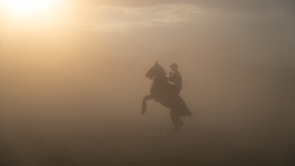 Unidentified man riding a horse in dust and fog