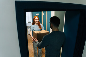 High-angle view of young woman receiving cardboard box from unrecognizable delivery man on doorstep...