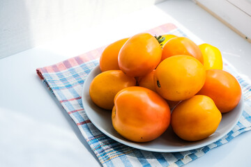 Orange organic tomatoes in a gray plate on a windowsill. Sunlight. Healthy nutrition. Harvest. Minimalistic simple natural neutral light template. Superfood. Organic eco health care. Vitamin nutrition