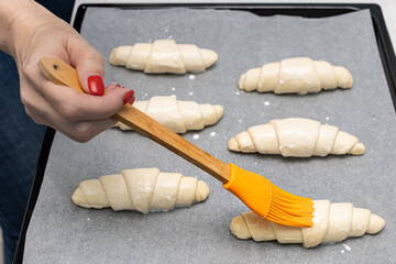 a woman's hand smears milk on a raw dough croissant
