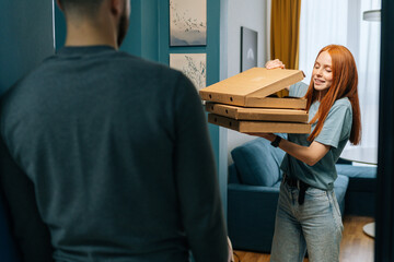 Happy hunger young woman open box of hot pizza standing at entryway on apartment, looking inside....