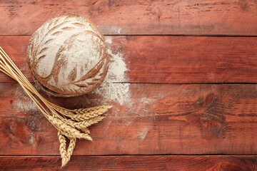 Round beautiful rye bread large, sprinkled with flour next to ears of wheat. Bakery concept, natural farm product. Background wooden red board.