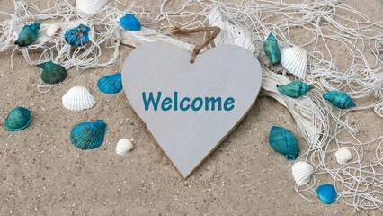 The word Welcome on a heart in the sand with seashells and starfish.