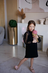Little angel baby girl with pink transparent wings. Little girl standing in black dress at home...