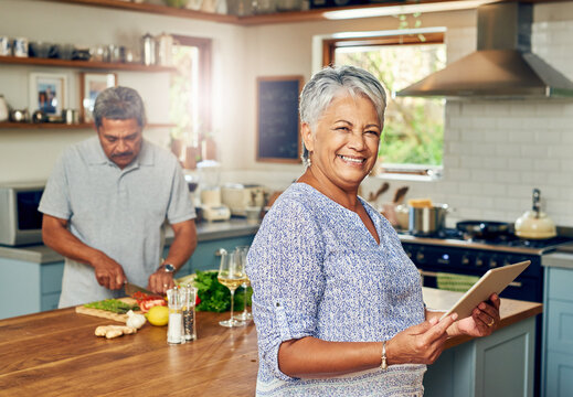 The smartest little soux chef there is. Portrait of a mature woman using a digital tablet while preparing a meal at home with her husband.