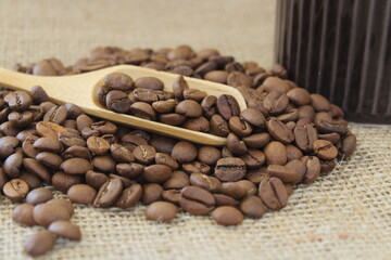 Roasted coffee beans in wooden scoop on brown burlap or sack cloth background.