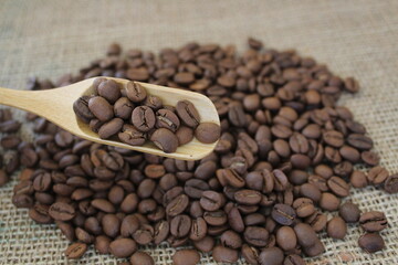 Roasted coffee beans in wooden scoop on brown burlap or sack cloth background.