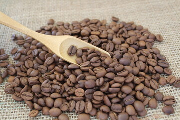 Roasted coffee beans in wooden scoop on brown burlap or sack cloth background.
