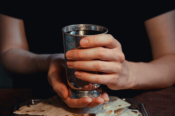 Women's hands hold a cup of wine over a dish of bread for the Easter church rite of communion