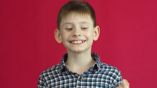 Portrait of a cheerful Caucasian boy 7 years old rejoicing that he removed a sick milk swinging tooth.Studio shooting on a red background. Joyful child pulled out a milk tooth