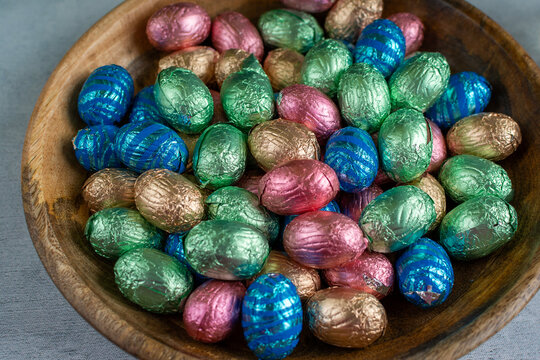 Colorful foil wrapped easter eggs in wooden bowl
