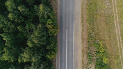 Top view of dividing line of forests and fields. Scene. Cars are driving on country highway with forest strip. Highway divides forest zone and field