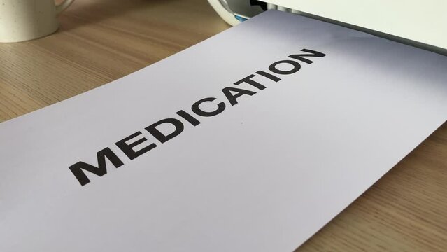 Printing &ldquo;MEDICATION&rdquo; black text written message word on paper sheet A4 document. Close up page being printed from multifunction printer scanner in office. Hand take paper from printer