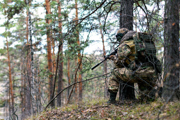 Military invasion - a soldier during a clash in the forest on enemy territory. He aims at the enemy from an ambush. Concept of modern warfare and special forces.