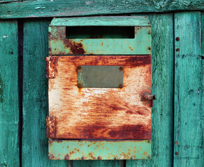old rusty metal mailbox with a slot to drop letters, hanging on a green painted wooden door or fence - rural textured scene as a symbol of abandonment and loneliness