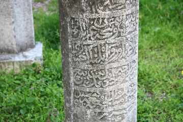 closeup white stone post carved with islam religious inscriptions with arabic symbols on the tombstone in a muslim cemetery, with grass around in background