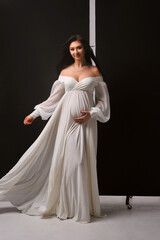 Studio portrait of attractive pregnant woman in white dress on black background. Dress is fluttering