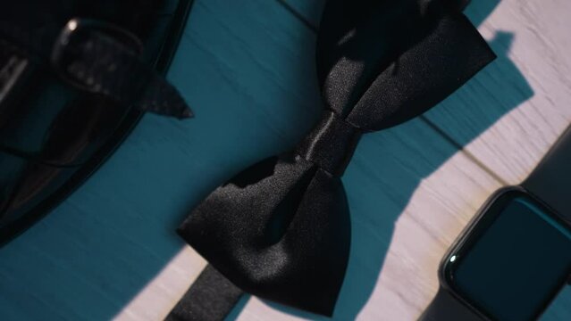 Men's accessories on the floor are isolated. Luxurious exquisite details of men's wardrobe. Leather shoes and belt with metal buckle, stylish classic cufflinks, wristwatch and bow tie. Twisting camera