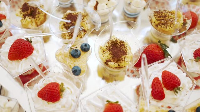 Sweet buffet table. Cream desserts are laid out in layers in plastic cups and decorated with fresh organic strawberries and blueberries. Disposable spoon in each vessel. Self-service