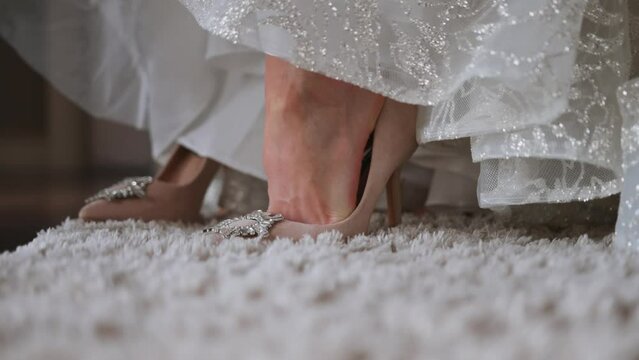 On the wedding day, a woman in a wedding dress stands barefoot on the carpet and puts on high-heeled shoes. The bride had a problem with wearing shoes and her dad helped her put the shoe on