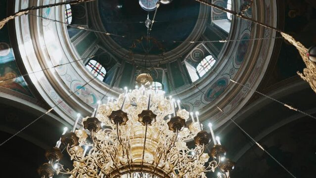 Ukraine, Lviv - August 5, 2021: Interior of church. Chandelier with light shining on background of dome-shaped ceiling. Holy apostles and God are depicted on ceiling. Spirituality and religion