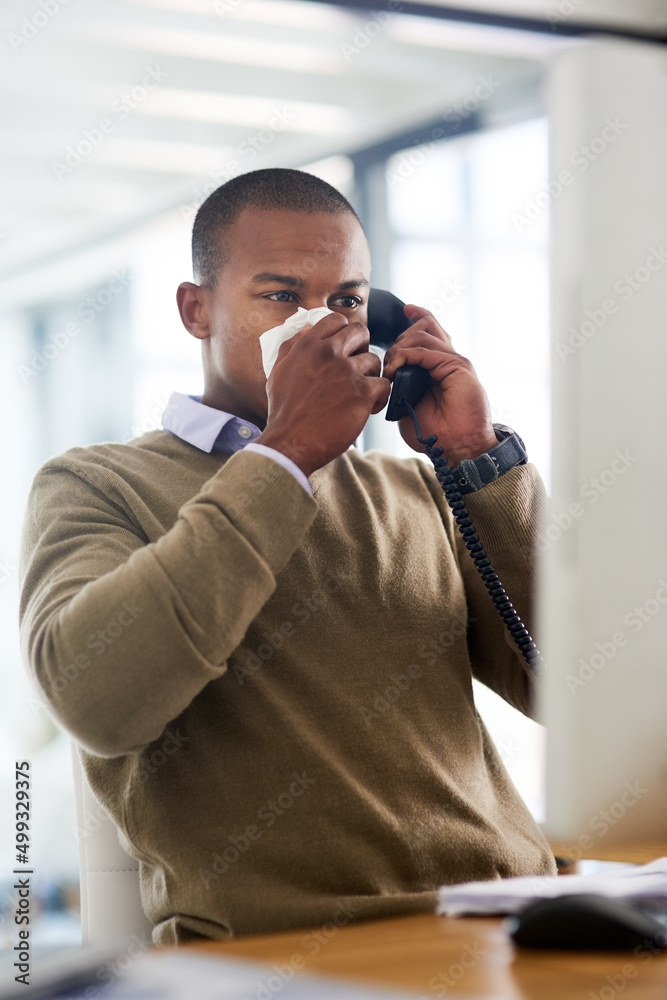 Sticker making an appointment to see his gp. shot of a young businessman blowing his nose at his work desk.