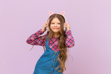 A joyful little girl in headphones and a denim skirt on an isolated background.