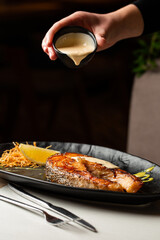 One piece of baked salmon steak grilled lemon and salt on a dark plate decorated with white sauce