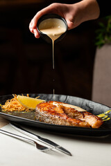 One piece of baked salmon steak grilled lemon and salt on a dark plate decorated with white sauce