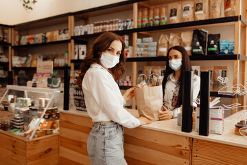 Fototapeta na wymiar Girl buyer in a mask makes a purchase in the store. Saleswoman or small business owner wearing medical mask at the counter in cafe or small shop.