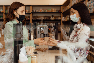 A young girl in a mask buys coffee to go. Health care and technology concept during coronavirus pandemic