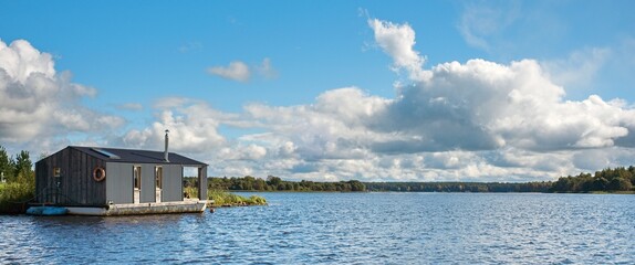 A modern houseboat in an open river landscape. The concept of summer holidays near the river. Wide banner, copy space.