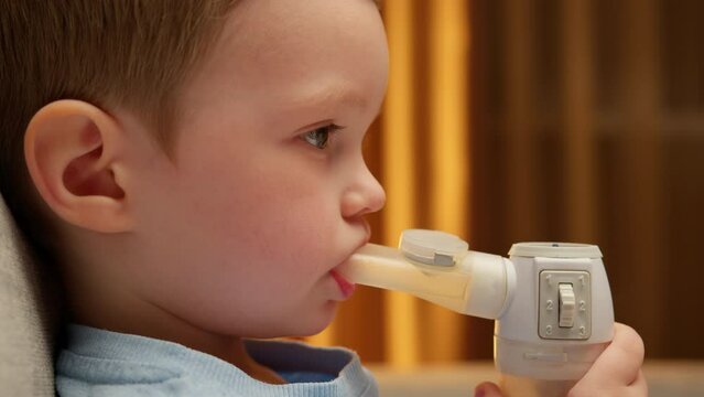 Portrait Caucasian Child With Asthma Problems Inhales With Tube In His Mouth. Treatment Of Pneumonia With Nebulizer At Home. Child Has Respiratory Infection Or Bronchitis, And He Is Breathing Heavily.