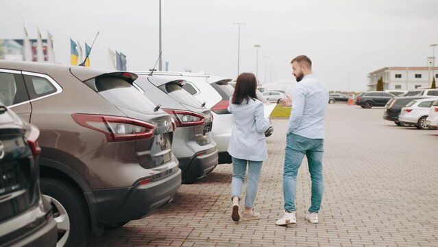 Caucasian man standing with female seller near modern car with sale banner on windshield. Male customer choosing new vehicle with help of comeptent dealer. Talking with saleswoman about car outdoors.
