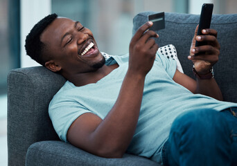 I always get the best deals. Shot of a young man using a credit card and phone on the couch at home.